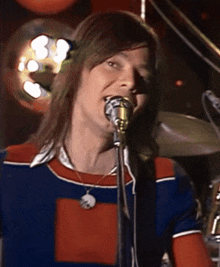 a man singing into a microphone with a necklace that says ' a ' on it