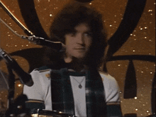 a man wearing a plaid shirt and a necklace is playing drums