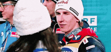 a man wearing a red bull giesswein hat stands next to a woman