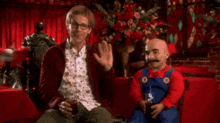 a man sitting next to a man dressed as mario waving
