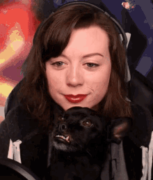 a woman with red lipstick holds a small black dog in her lap