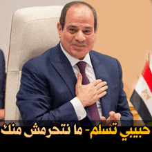 a man in a suit and tie holds his hand to his chest with arabic writing behind him