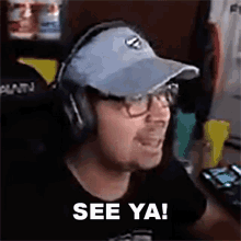 a man wearing headphones and a hat is sitting at a desk and says see ya !