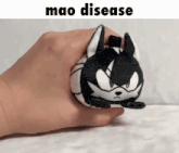 a person is holding a black and white stuffed animal with mao disease written above it