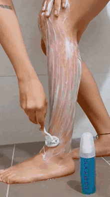 a woman is shaving her leg with a razor next to a bottle of aquafina lotion