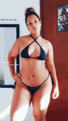 a woman in a black bikini is standing in front of a wall with a picture of a man on it