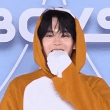 a young man wearing a yellow hoodie and a white glove is covering his mouth .