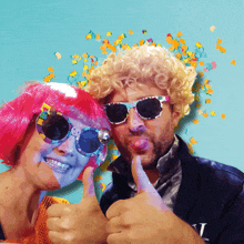 a man and a woman wearing colorful wigs and sunglasses are giving a thumbs up