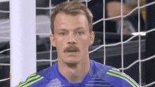 a man with a mustache wearing a blue and yellow adidas shirt