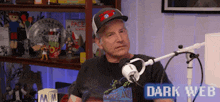 a man wearing a hat is sitting in front of a microphone with the words dark web above him