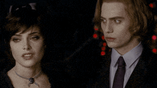 a man in a suit and tie stands next to a woman in a necklace