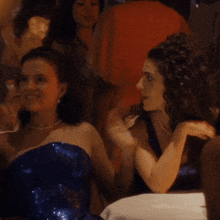 a woman in a blue dress laughs with another woman in a black dress