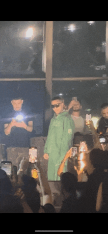 a man in a green jacket stands in front of a crowd of people
