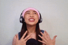 a woman wearing headphones and a pink hat is smiling and looking up .