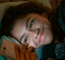 a woman is laying on a bed looking at her phone and smiling