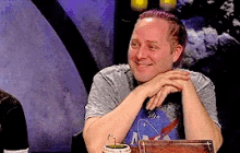 a man with purple hair is smiling and sitting at a table