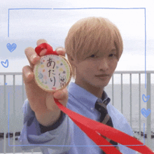 a man in a blue shirt and tie holds up a medal with a red ribbon around it