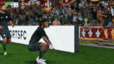 a soccer player squats in front of a banner that says fort fc