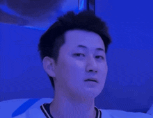 a man in a white shirt is making a funny face in front of a blue wall