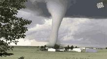 a tornado is moving through a field with a house in the background .