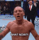 a shirtless man is standing in front of a crowd with his mouth open and says what now .
