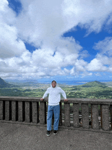 a man wearing a white hoodie stands on a ledge overlooking a valley