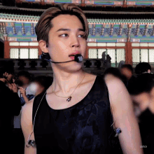 a young man wearing a black tank top and a microphone looks at the camera