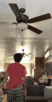 a man in a red shirt stands in front of a ceiling fan in a living room