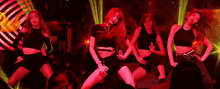 a group of women are dancing in a dark room with red lights behind them