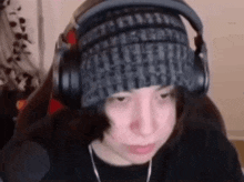 a person wearing headphones and a beanie is sitting in front of a computer screen .