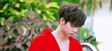a young man in a red robe is standing next to a fence .
