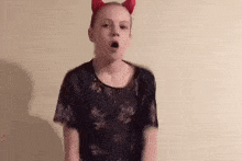a young girl wearing devil horns and a black shirt is making a funny face .