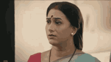 a woman with a red dot on her forehead is wearing a pink and blue saree and earrings .