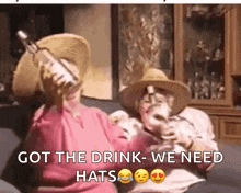 a man and a woman are sitting on a couch drinking wine while wearing hats