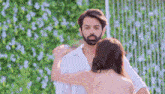 a man and a woman are hugging each other in front of a hedge .