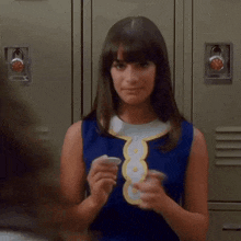 a woman in a blue dress is standing in front of lockers holding a cup