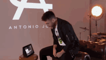 a man sits on a couch in front of a wall that says antonio jc