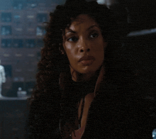 a woman with curly hair and a choker around her neck looks at the camera