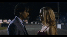 a man in a suit and tie and a woman in a pink dress are kissing in a parking lot at night .