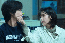 a man and a woman are looking at each other and the man is wearing a michikound sweatshirt