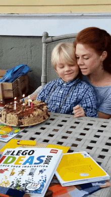 a woman and child sit at a table with a lego ideas book on it