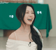 a woman wearing a white off the shoulder top is smiling in front of a green cloth that says september