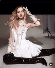 a woman is sitting on the floor wearing a white dress and black boots .