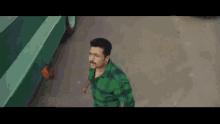 a man in a green shirt with a mustache is walking down the street .