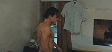 a shirtless man is standing in a room in front of a fan .