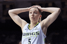 a female basketball player for the dallas wings holds her head in her hands