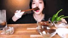 a woman is eating a piece of meat with chopsticks while sitting at a table
