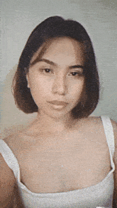a woman with short hair and a white tank top looks at the camera