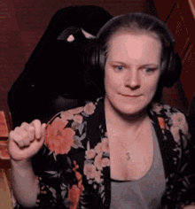 a woman wearing headphones and a floral shirt is sitting in a chair and making a fist .