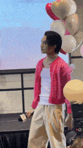 a man in a pink cardigan stands on a stage